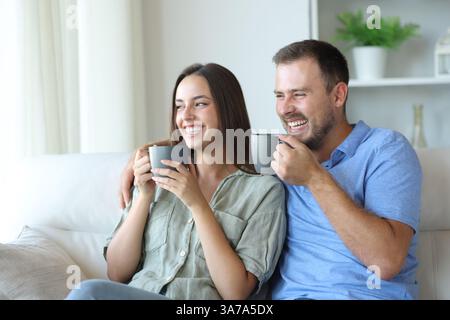 Coppia felice sorridente e bevendo un caffè seduto su un divano a casa Foto Stock