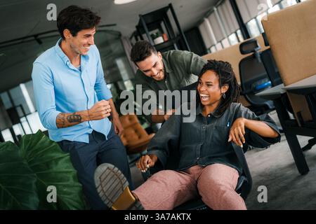 I giovani colleghi si divertono insieme a cavalcare sulle sedie in ufficio e lavorare in ufficio con persone molto eccitate Foto Stock