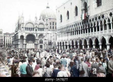 La folla riempie Piazza San Marco a Venezia, mostrando un vivace mix di gente del posto e turisti che si godono una giornata vivace. Realizzato nel luglio 1965 su pellicola slide da 35mm. Foto Stock