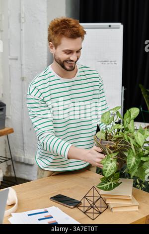 Un uomo svuota una pianta in vaso in un ufficio moderno, portando il verde nello spazio. Foto Stock