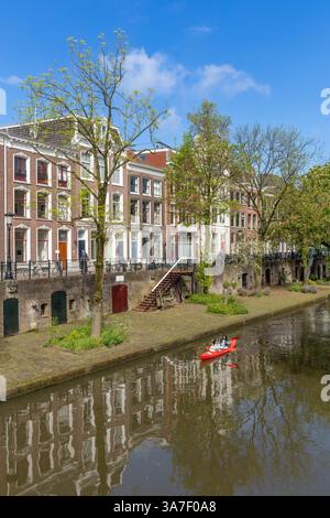 Canale di Oudegracht visto da un ponte. gente che canta una canoa rossa attraverso il canale. tradizionali case in mattoni di pietra lungo lo stato con biciclette Foto Stock