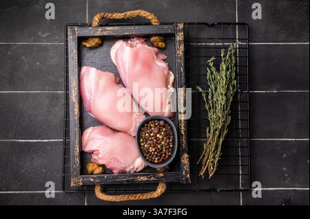 Filetti di cosce di pollo crude in un vassoio di legno fondo nero. vista dall'alto. Foto Stock