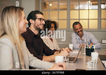 Un giovane uomo d'affari sorridente seduto con colleghi di sesso femminile nella sala riunioni dell'ufficio Foto Stock