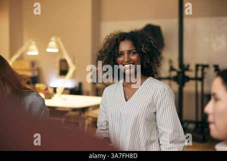 Ritratto di un professionista creativo dai capelli ricci sorridenti in piedi in ufficio Foto Stock