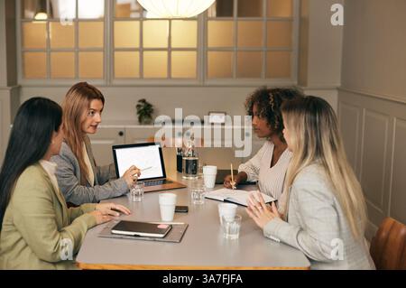 Donna d'affari che spiega le strategie alle colleghi mentre siede in una sala riunioni in ufficio Foto Stock