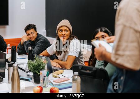 Giovane donna che discute con uno studente mentre siede in classe durante una riunione al college Foto Stock