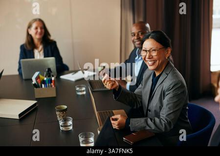 Donna d'affari matura e felice seduta con un computer portatile nella sala riunioni dell'ufficio Foto Stock