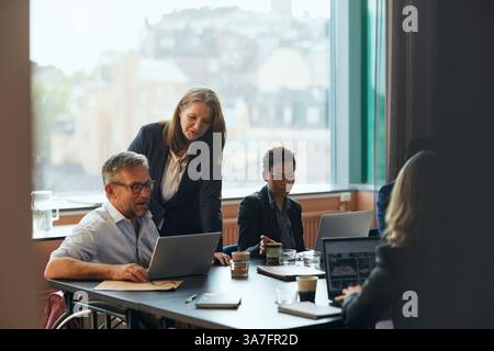 Imprenditrice donna che parla in videochiamata tramite notebook con un collega uomo con disabilità fisica in ufficio Foto Stock