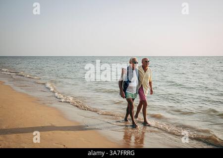 Coppia gay senior che cammina sulla costa della spiaggia sotto il cielo limpido Foto Stock