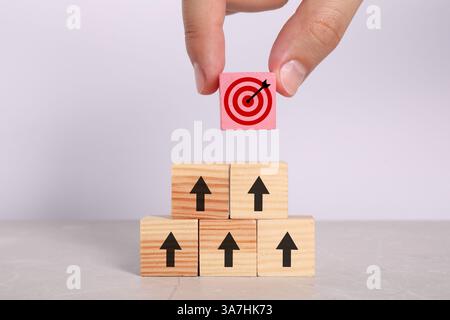 Targeting. Donna che mette un cubo rosa con un bullo sulla piramide di altre con frecce sul tavolo, primo piano Foto Stock