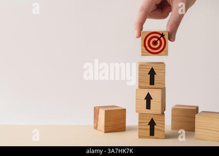 Targeting. Donna che mette il cubo con il buseye sopra gli altri con frecce sul tavolo di legno, primo piano Foto Stock