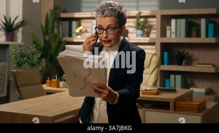 Arrabbiato arrabbiato furioso stressato dai capelli grigi anziano donna d'affari donna d'affari capo donna imprenditrice che tiene documenti segnala un errore Foto Stock