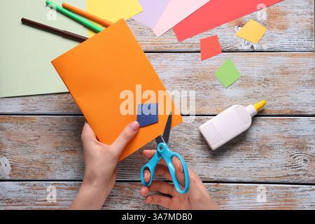 Donna che taglia carta arancione al tavolo di legno, vista dall'alto. Artigianato artigianale per bambini Foto Stock