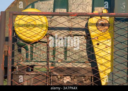Vista ravvicinata delle apparecchiature industriali con ingranaggi gialli e rete protettiva, illuminata dalla luce solare dorata. L'immagine acquisisce la trama A. Foto Stock