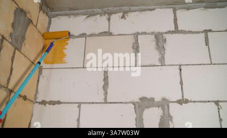 Applicazione di un primer arancione alla parete. Primer colorato per pareti. Locali, fase manuale dei lavori di ristrutturazione. Adescare la parete con un rullo arancione. Foto Stock