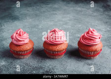 Yummy cupcakes colorati con panna montata in tazze di carta rossa decorata con corda rossa posta sul tavolo grigio Foto Stock