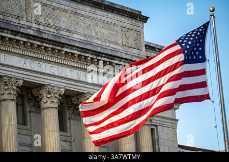 WASHINGTON DC - la bandiera americana vola di fronte al quartier generale del Dipartimento dell'Agricoltura degli Stati Uniti a Washington DC. Completato nel 1930, il Jamie L. Whitten Federal Building esemplifica lo stile architettonico Beaux-Arts con la sua classica facciata in pietra calcarea e colonne prominenti. L'USDA Administration Building occupa una posizione significativa vicino al National Mall lungo Independence Avenue e ospita gli uffici del Segretario dell'Agricoltura e di altri dirigenti del dipartimento. Foto Stock