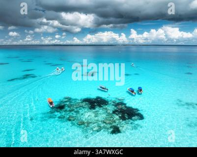 Vista aerea di barche colorate e yacht in acque cristalline nelle soleggiate giornate estive. Isola di Mnemba, Zanzibar. Vista dall'alto del banco di sabbia con la bassa marea, il mare blu e il nuoto Foto Stock