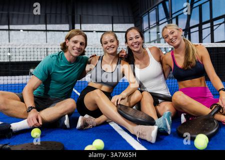 Gruppo di amici seduti sul campo sorridenti dopo la partita di tennis Foto Stock