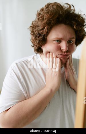 Giovane uomo che indossa una camicia bianca toccando il suo volto nel pensiero Foto Stock