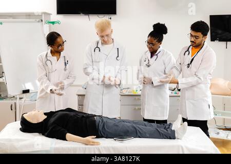 Quattro studenti di medicina che indossano guanti e cappotti bianchi praticano la RCP su un manichino medico durante una sessione di formazione Foto Stock