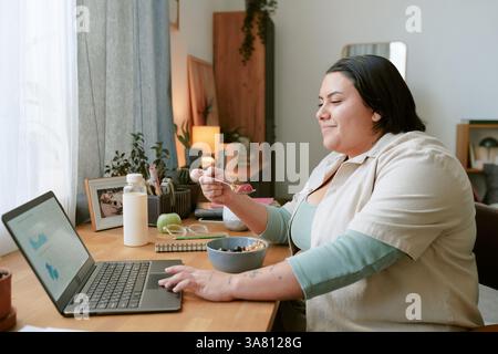 Donna afroamericana che si gode una sana colazione lavorando da remoto Foto Stock