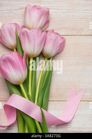 I tulipani rosa con nastro rosa sono adagiati su un tavolo di legno, creando una scena delicata e romantica Foto Stock
