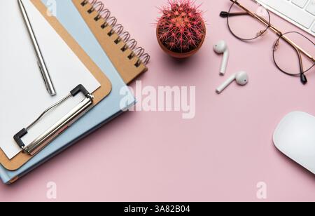 Forniture per ufficio e dispositivi tecnologici disposti in modo ordinato su un desktop rosa, creando uno spazio di lavoro ideale per la produttività e la concentrazione Foto Stock