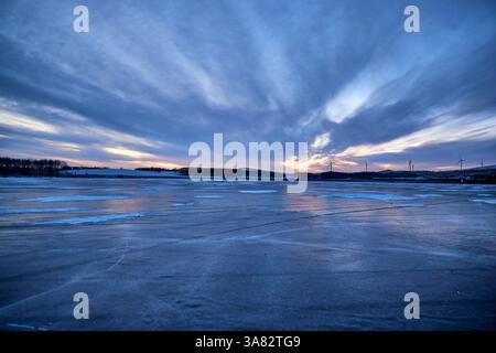 Tramonto invernale su un lago ghiacciato con turbine eoliche Foto Stock