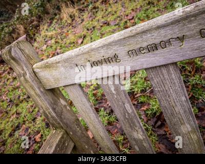 Panca in legno con ‘in Loving Memory’ intagliata nello schienale, situata in un tranquillo parco invernale Foto Stock