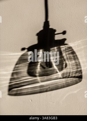 Ombra di una lampada a sospensione con paralume in vetro su una parete bianca, creando un'immagine morbida simile a quella di un carbone. Foto Stock
