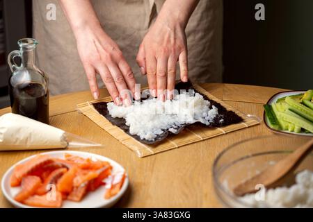 Preparare sushi a casa. Aggiungere riso su nori. Foto Stock