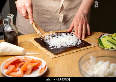 Preparare sushi a casa. Aggiungere riso su nori. Foto Stock