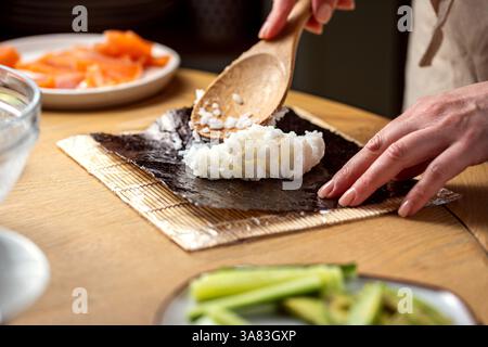 Preparare sushi a casa. Aggiungere riso su nori con un cucchiaio di legno Foto Stock