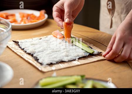Preparare sushi a casa. Aggiungere il salmone sui nori e crescere Foto Stock