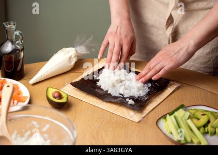 Preparare sushi a casa. Aggiungere riso su nori. Foto Stock