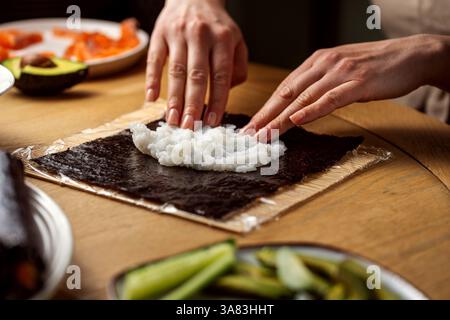 Mani che aggiungono riso su nori, preparano suhi fatti in casa Foto Stock