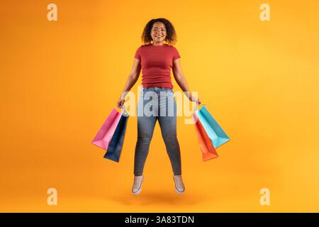Giovane donna afroamericana energica che salta con gioia con le colorate borse della spesa Foto Stock