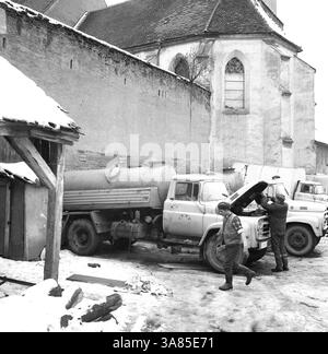 Medias, Contea di Sibiu, Repubblica Socialista di Romania, circa 1976. Uomini che mantengono camion di proprietà statale parcheggiati dietro il castello medievale. Foto Stock