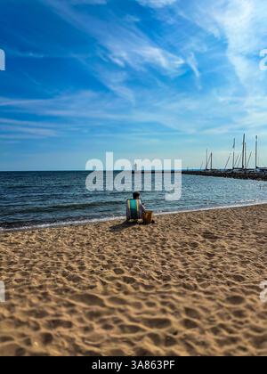 Donna che si rilassa su una sdraio sulla spiaggia con vista sul faro e sul porticciolo in una giornata di sole sul lago Vattern, Svezia. Foto di alta qualità. Foto Stock