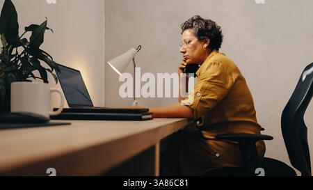 Una donna matura e professionale impegnata in una telefonata mentre lavora alla scrivania in un ufficio. Foto Stock