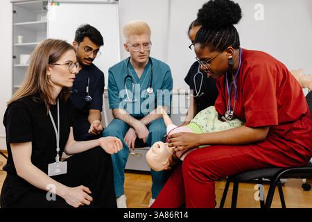Diversi gruppi di studenti di medicina che imparano le cure infantili su un manichino medico durante una sessione di formazione Foto Stock