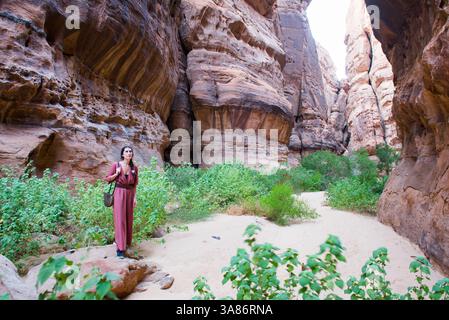 Donna che cammina sul fondo di un canyon con pareti di arenaria nella riserva naturale di Sharaan, Alula, provincia di Medina, Arabia Saudita Foto Stock