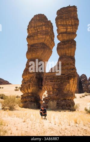 Un uomo che accosta accanto a una straordinaria struttura in pietra arenaria chiamata Dancing Rocks, Sharaan Nature Reserve, Alula, Medina Province, Arabia Saudita Foto Stock