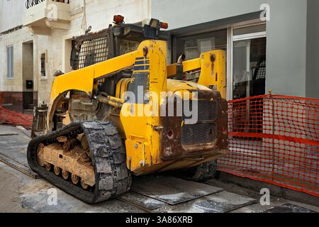 Vecchia minipala cingolata gialla in un cantiere urbano. Tracce ruvide, in metallo graffiato, ricoperte di sporcizia. Foto Stock