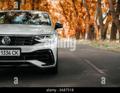 Silver Volkswagen Tiguan su una strada forestale il giorno d'autunno. Vista ravvicinata di un lato anteriore sinistro della vettura su una strada alberata rurale. Foto Stock
