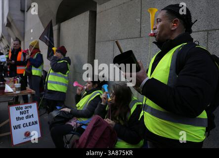 Londra, Regno Unito. 27 marzo 2025. Un membro sulla linea del picchetto soffia un kazoo e sbatte una campana di mucca. Lavoratori, membri della Cleaners and Allied Workers Union (CAIWU) picchetto fuori dalla Central London Criminal Court (Old Bailey) in Newgate Street, Londra. Essi si oppongono alla privatizzazione dei loro posti di lavoro. La City of London Corporation sta progettando di trasferirli a nuovi contratti in outsourcing. I lavoratori temono per il loro futuro e sostengono che ciò comporterà retribuzioni inferiori e carichi di lavoro più pesanti. (Foto di Martin Pope/SOPA Images/Sipa USA) credito: SIPA USA/Alamy Live News Foto Stock