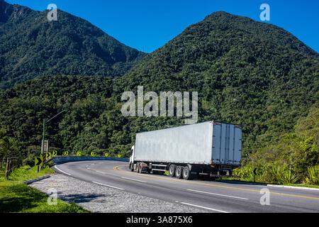 La strada RJ-116 attraversa una striscia di foresta atlantica primaria tra Nova Friburgo e Cachoeiras de Macacu nello stato di Rio de Janeiro, Brasile, sottolineando il delicato equilibrio tra le esigenze di trasporto regionale e la conservazione ambientale. L'autostrada tortuosa fornisce una connettività vitale tra le città che dipendono dal turismo e dal commercio, mentre gli ambientalisti sottolineano la protezione di questa foresta montana biodiversificata, sede di specie endemiche e di ecosistemi cruciali che sequestrano il carbonio, dalla frammentazione e dal degrado. Foto Stock