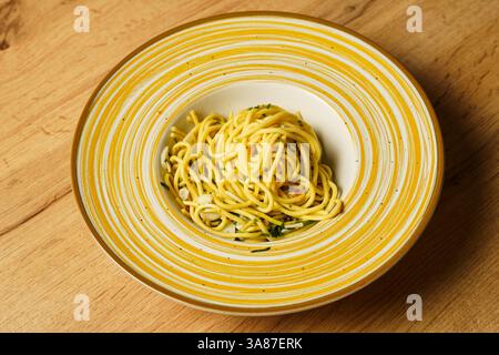 Una porzione splendidamente placcata di spaghetti aglio e olio, guarnita con prezzemolo fresco e aglio a fette sottili. La pasta risplende di olio d'oliva e h Foto Stock