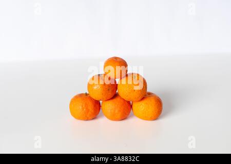 Uno studio fotografico ravvicinato mostra una piramide ben impilata di mandarini freschi su uno sfondo bianco e pulito. Le vivaci arance forniscono un stri Foto Stock